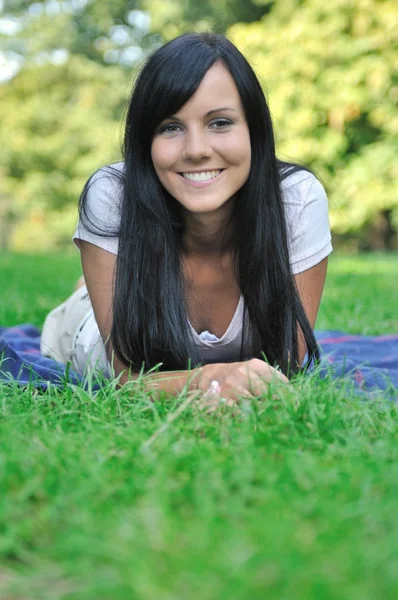 Mladá usměvavá žena ležící v trávě venku — Stock fotografie
