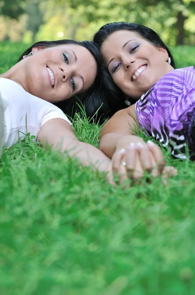 Две улыбающиеся сестры лежат на улице в траве, держась за руки — стоковое фото