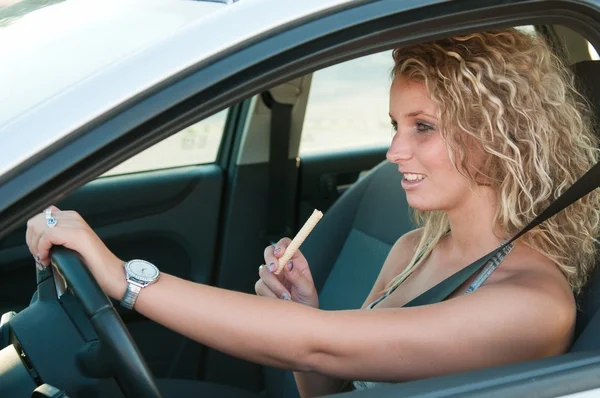 Молодая женщина ест сладости за рулем автомобиля — стоковое фото