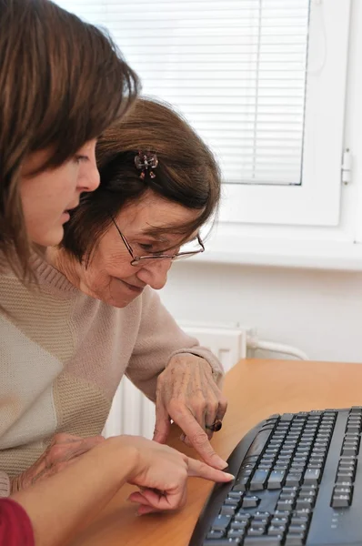 Mujer joven enseña a su abuela a trabajar con la computadora — Foto de Stock