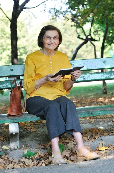 Äldre kvinna läser bok autdoors — Stockfoto