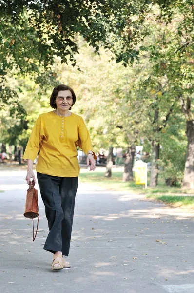Smiling senior woman wlaking in park — Stock Photo, Image