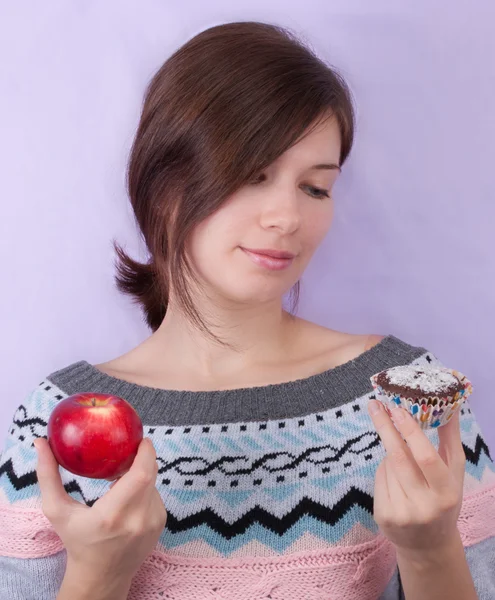 Девушка выбирает между яблоком и кексом — стоковое фото