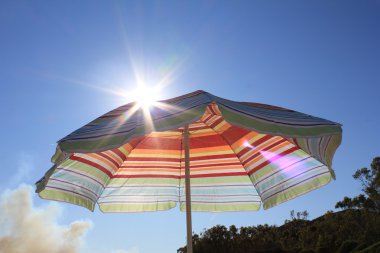 Colorful beach umbrella against sunny blue sky clipart