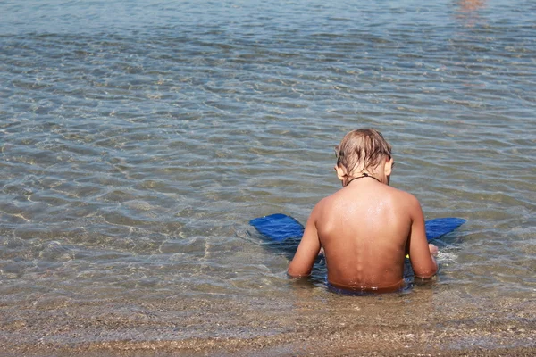 Poika istuu veden äärellä trooppisella rannalla — kuvapankkivalokuva