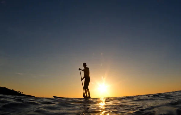 Günbatımında sörf tahtasına kürek çekmeye bir adam silüeti — Stok fotoğraf