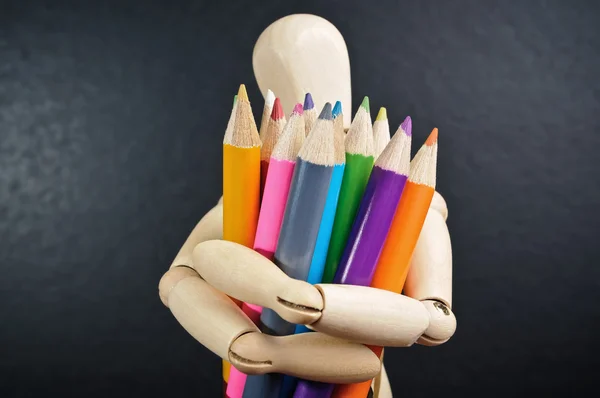 stock image Wooden mannequin holds in hand a set of color pencils