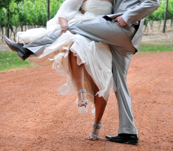 Bride and groom lifting legs on dust road — Stock Photo, Image