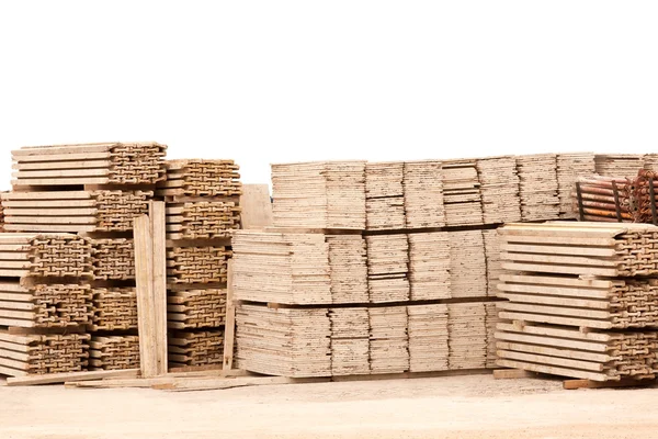 Pilha de tábuas de madeira no chão de cascalho contra a parede branca — Fotografia de Stock