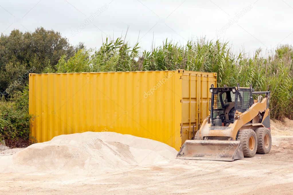 Excavator and a container near a pile of gravel against con field