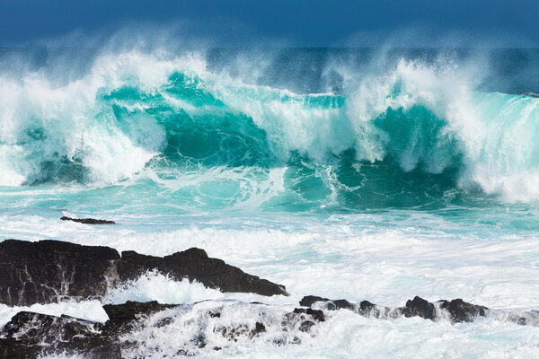 Turquoise rolling wave slaming on the rocks