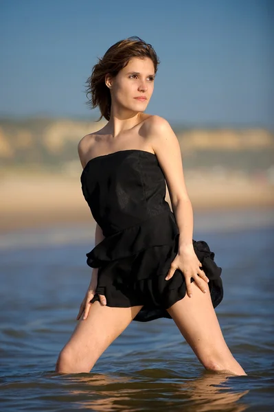 Giovane bella donna in un abito nero in spiaggia — Foto Stock