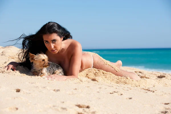 Brunette femme à la plage couché dans le sable avec un chien — Photo