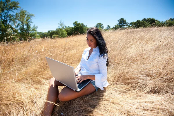 Όμορφη γυναίκα που εργάζεται σε ένα φορητό υπολογιστή στη μέση ενός χωραφιού — Φωτογραφία Αρχείου
