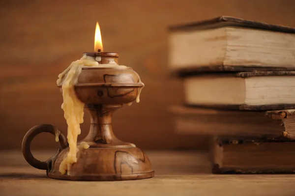 Tahta bir masada eski bir mum, arka planda eski kitaplar. — Stok fotoğraf