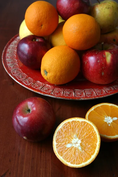 Jabłka i pomarańcze na płytce czerwony — Zdjęcie stockowe