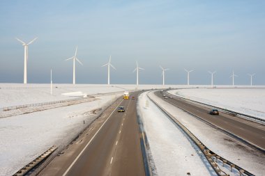 Dutch highway in wintertime with wind turbines behind it clipart