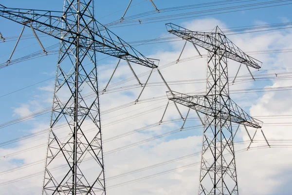 Dois postes de eletricidade contra um céu azul nublado — Fotografia de Stock