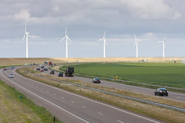Auto-estrada com uma linha de grandes turbinas eólicas atrás dela — Fotografia de Stock