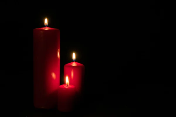 Набор из трех красных свечей, горящих в темноте — стоковое фото