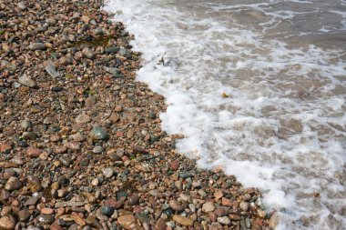 Wave breaking at the beach with many coloured pebbles, France