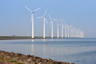 Windmills along the coastline, mirroring in the calm sea. clipart