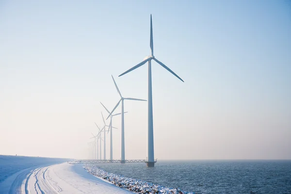 Rij van besneeuwde windmolens permanent in Nederlandse zee verdwijnen in win Stockfoto