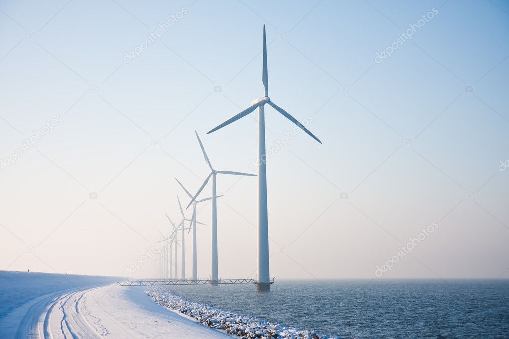 Row of snowy windmills standing in Dutch sea disappearing in win
