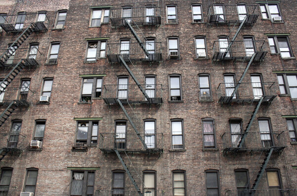 A brick apartment building in New York City with many windows and fire escapes