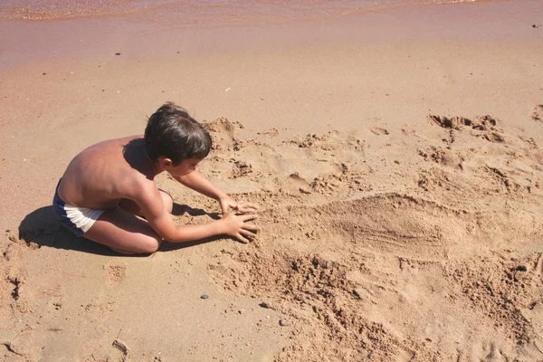 Çocuk kum üzerinde bir rakam oluşturmak yoluyla. — Stok fotoğraf