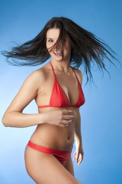 Heldere brunette in een rode badpak op een blauwe achtergrond — Stockfoto