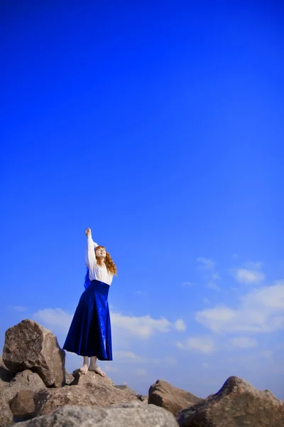 Meisje in een blauwe jurk tegen een achtergrond van de blauwe hemel — Stockfoto