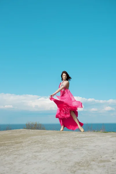 Flicka i rosa klänning mot bakgrund av himlen. — Stockfoto