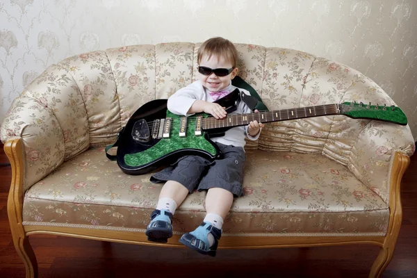 Mały chłopiec moda gitarzysta siedzi na kanapie Glamour — Zdjęcie stockowe