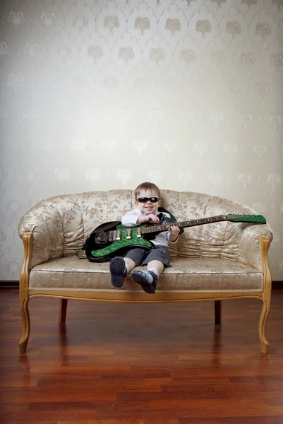 Piccolo ragazzo chitarrista seduto sul divano glamour — Foto Stock