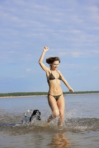 美丽细长的女孩和一只狗在沙滩上玩 — 图库照片