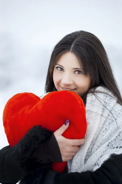 Красивая девушка в зимнем лесу с красным сердцем — стоковое фото