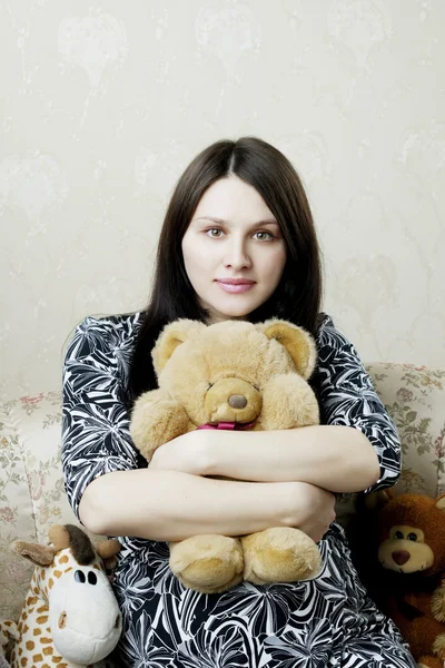 Беременная женщина сидит на винтажном диване с игрушками — стоковое фото
