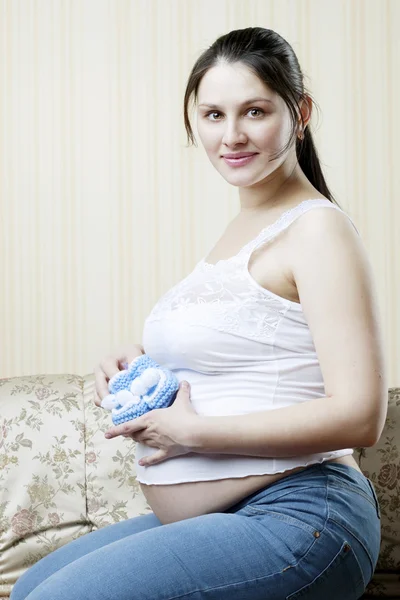 Schwangere auf der Couch mit blauen Booties in den Händen von — Stockfoto
