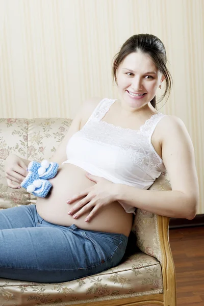 Femme enceinte sur le canapé avec des chaussons bleus dans les mains de — Photo