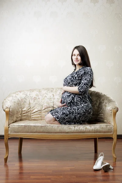Pregnant woman sitting on a vintage couch — Stock Photo, Image
