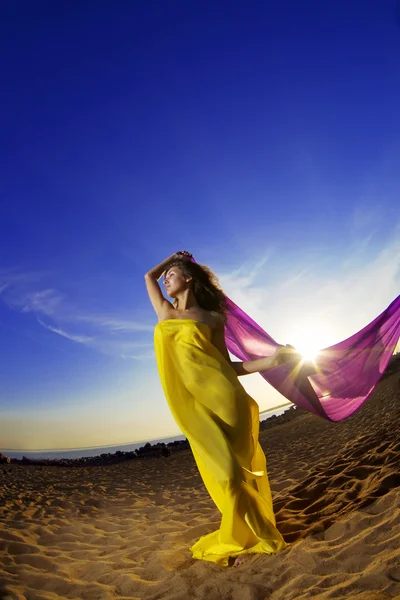 Menina na praia tecido crescente em um fundo do sol . — Fotografia de Stock