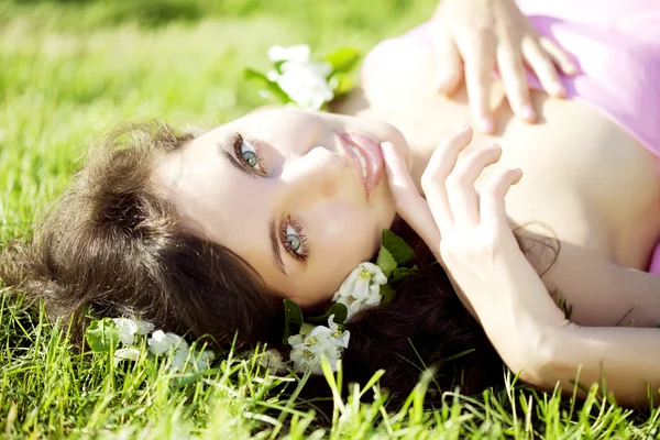 Menina bonita deitada na grama com flores — Fotografia de Stock