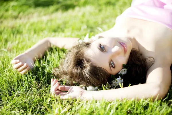 Menina bonita deitada na grama com flores — Fotografia de Stock