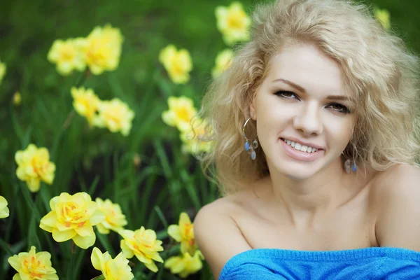 Krásná pozitivní dívka v parku, obklopen květy — Stock fotografie