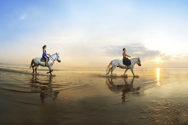 Влюбленная пара, которая скачет на коне по морю на солнце — стоковое фото