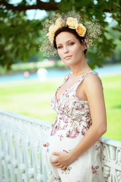 Mooie zwangere meisje met een krans van bloemen — Stockfoto