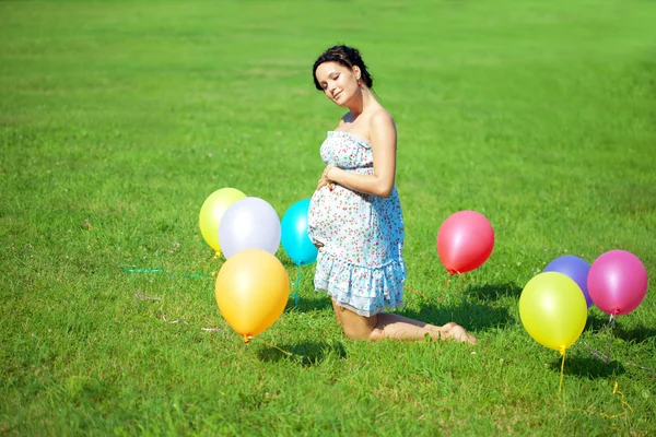 Těhotná žena s balónky na trávě — Stock fotografie