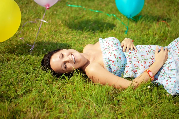 Těhotná žena s balónky na trávě — Stock fotografie