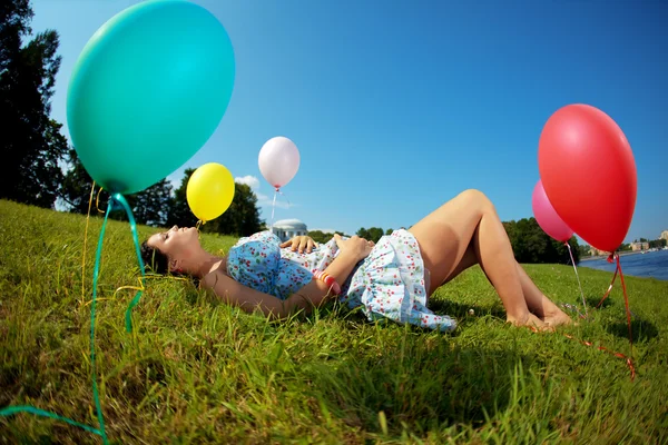 Беременная женщина с шариками на траве — стоковое фото
